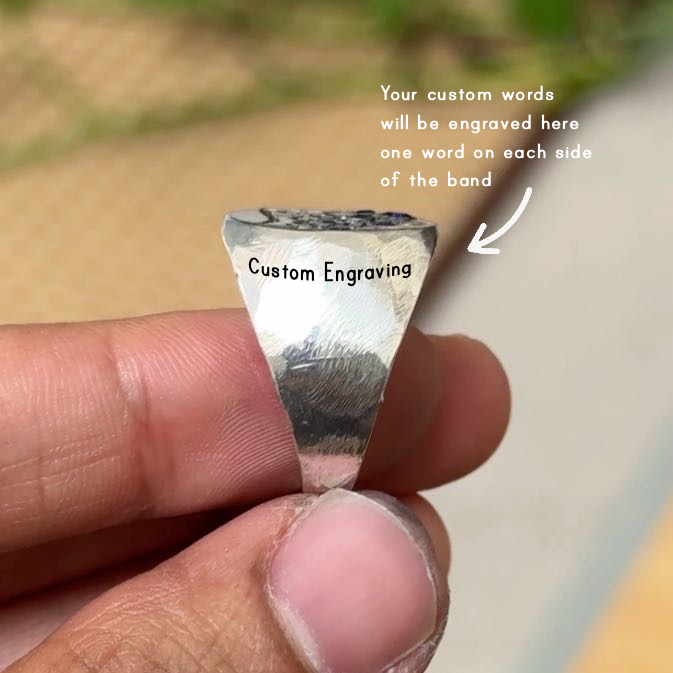 A close-up of a hand holding a triangular silver band engraved with the words 'Custom Engraving'. White text on the right explains that custom words will be engraved on each side of the band, with a pointing arrow.