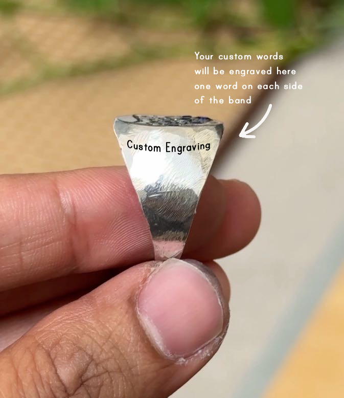 A close-up of a hand holding a triangular silver band engraved with the words 'Custom Engraving'. White text on the right explains that custom words will be engraved on each side of the band, with a pointing arrow.