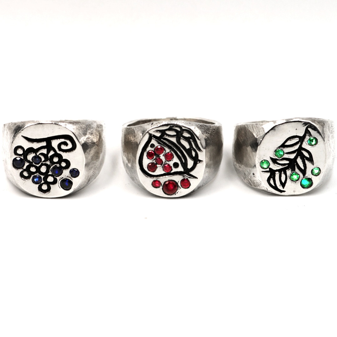 Three wide silver rings with black vine and berry motifs, decorated with small colored stones in blue, red, and green, displayed on a white background.